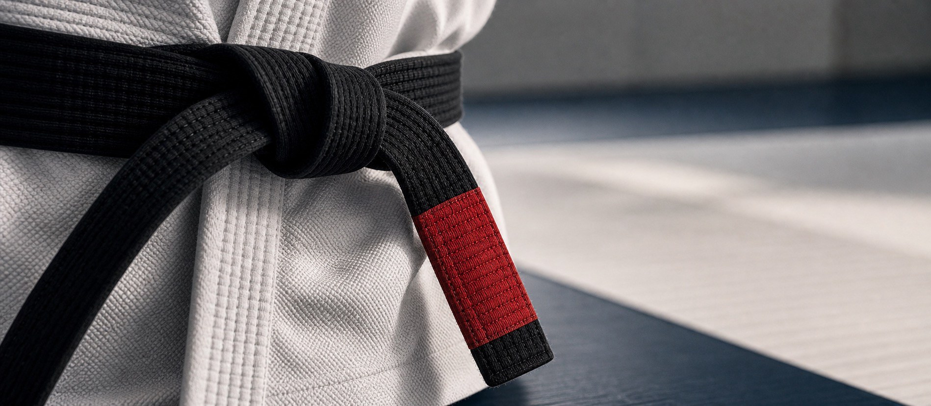 Brazilian Jiu Jitsu black belt with red bar on a dark mat